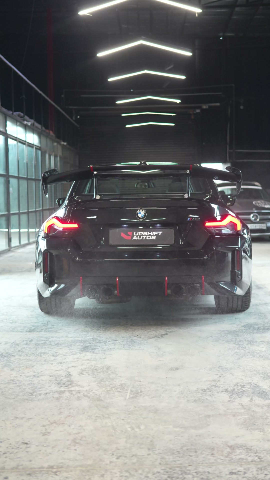 Rear of a black BMW M2 with exhaust haze in the workshop hall