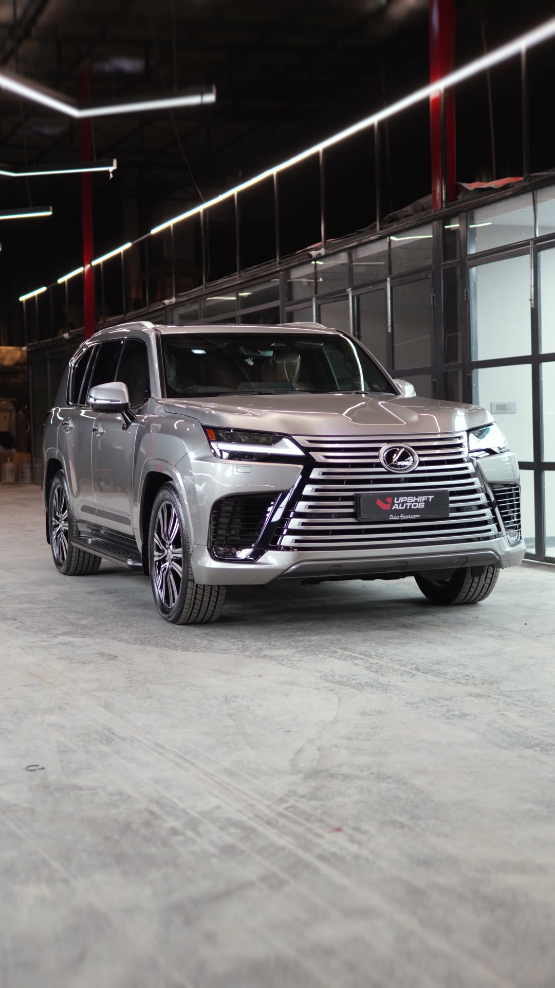 A silver Lexus LX500d, front three-quarter view in the workshop hall under strip lights.