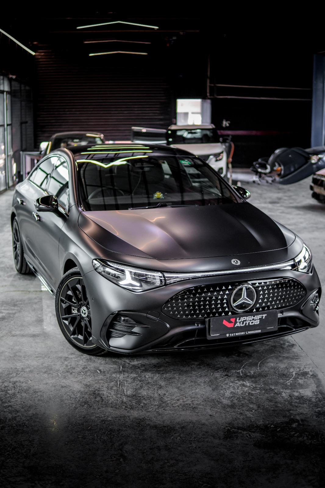 A Mercedes-Benz EQE in matte grey with its star-pattern grille panel, low front three-quarter view in the workshop.