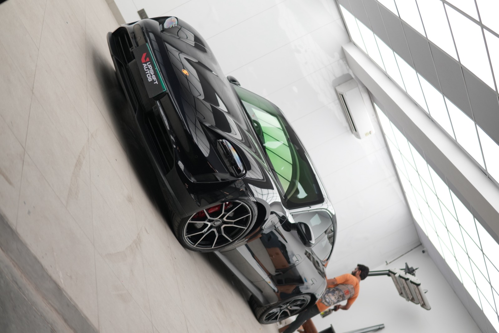 A black Porsche Taycan, low front three-quarter view, in a bright white-walled bay while a technician works at the rear door.